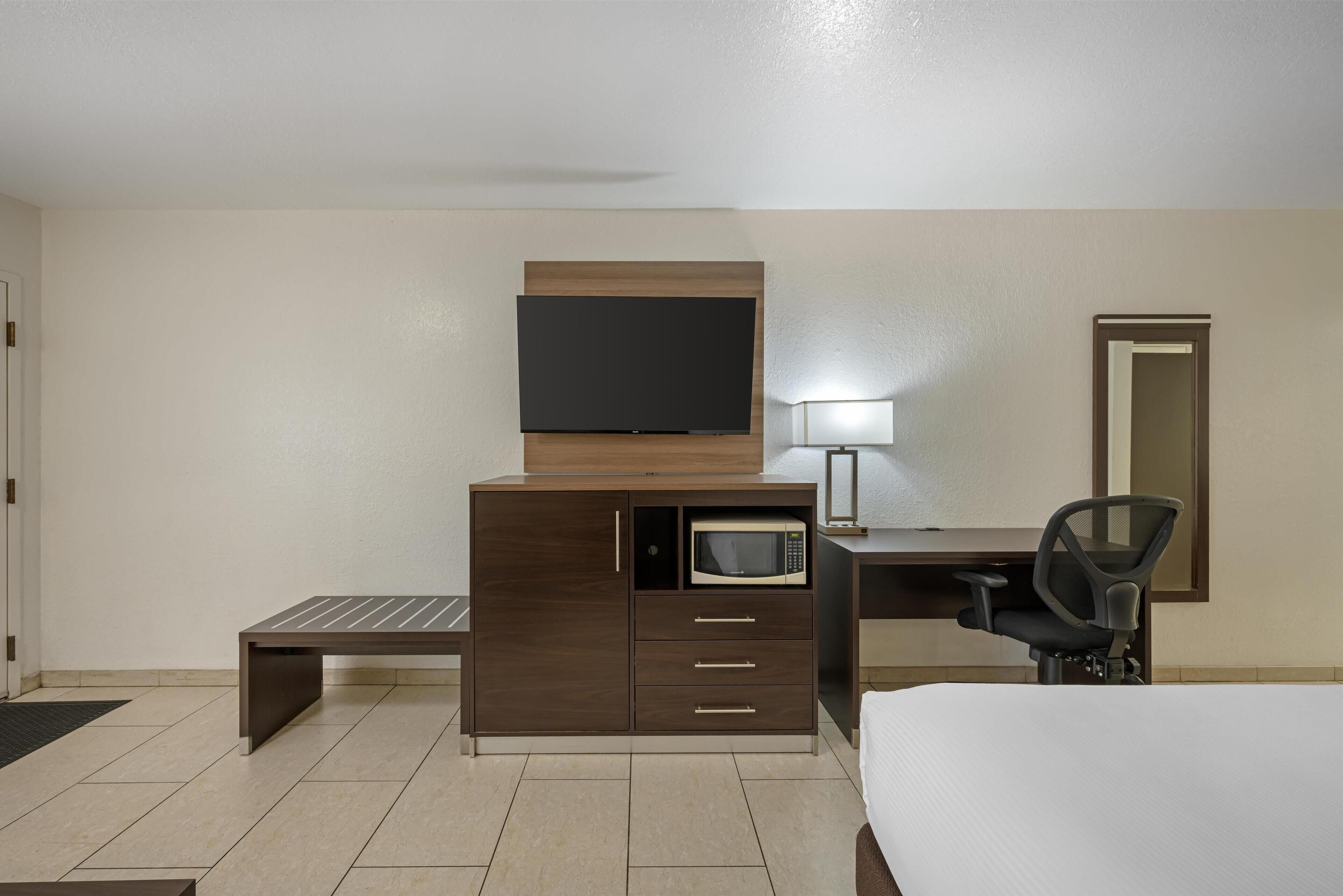 Habitación de hotel con cama, escritorio con computadora, microondas, televisión y una silla.