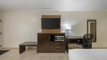 Habitación de hotel con cama, escritorio con computadora, microondas, televisión y una silla.