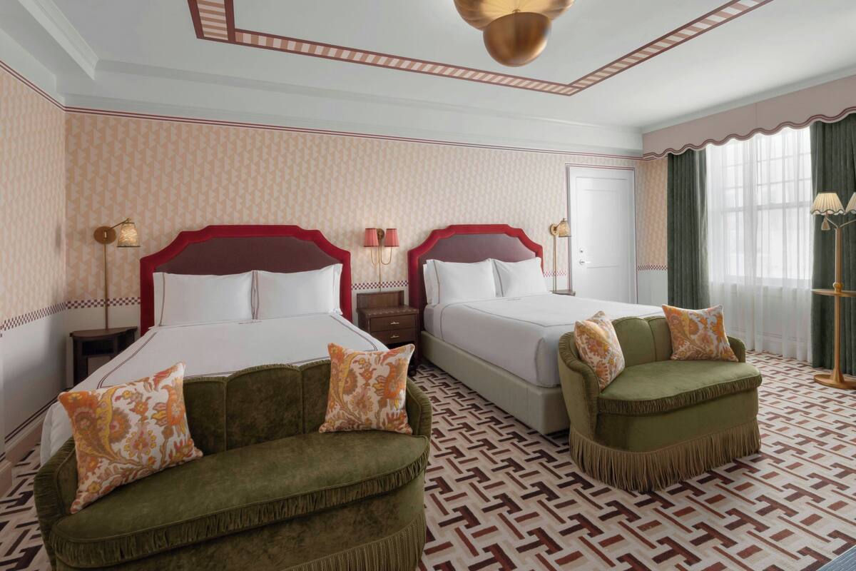 Ett hotellrum med två sängar, en grön soffa, tapet med mönster och ett mönstrat golv.