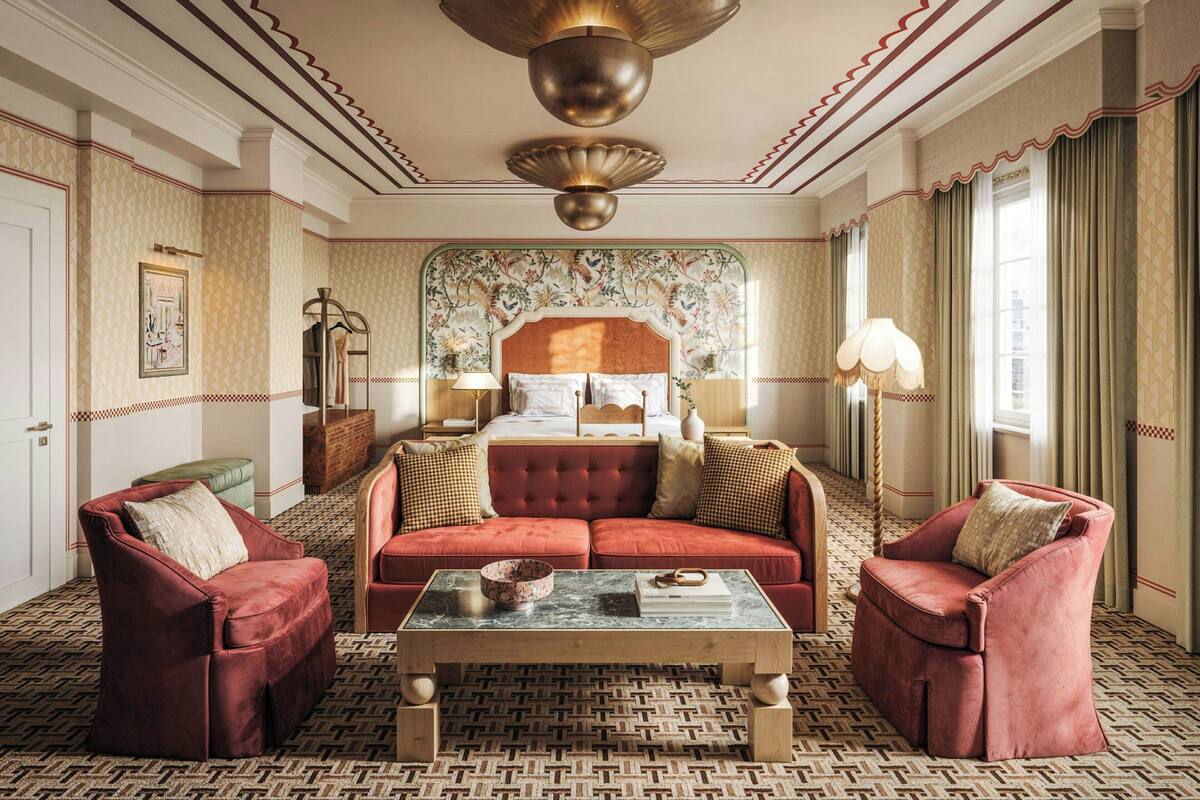 Ett hotellrum med en stor säng, två röda fåtöljer, ett träbord och ett golv med ett mönster.