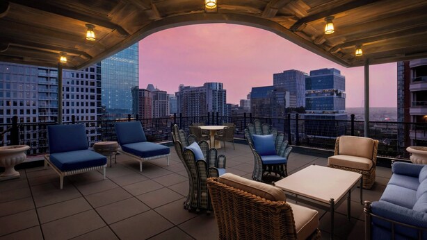 A rooftop terrace with outdoor seating, a view of the city skyline, and a wooden ceiling structure. - The Stoneleigh, Autograph Collection (Dallas)