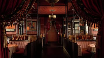 Un pasillo tenuemente iluminado con candelabros ornamentados, cortinas rojas y asientos con diseños.