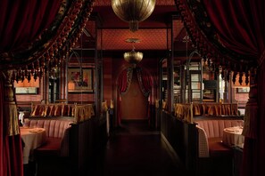 A dimly lit corridor with ornate chandeliers, red curtains, and patterned seating. - The Stoneleigh, Autograph Collection (Dallas)