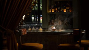 A bar area with a counter, stools, and shelves of bottles. - The Stoneleigh, Autograph Collection (Dallas)