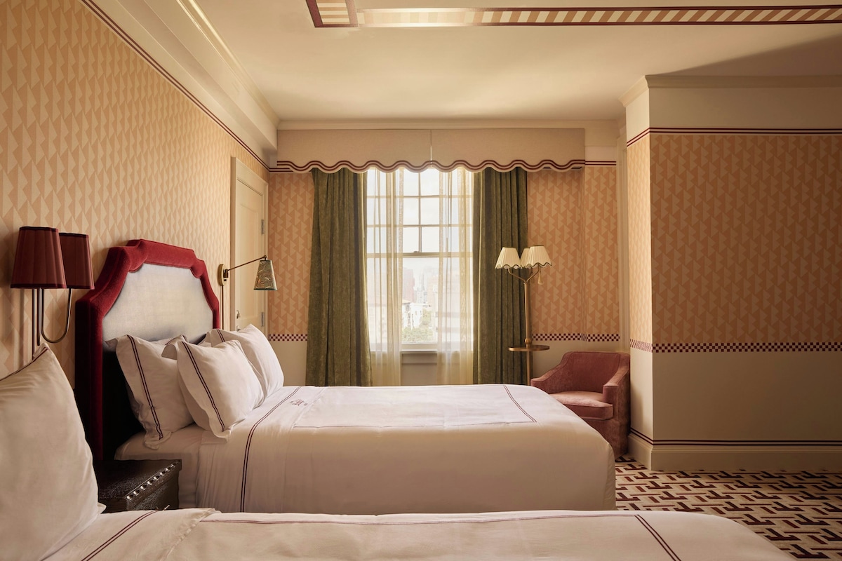 A hotel room with a large bed, a chair, a desk, and a window with curtains.