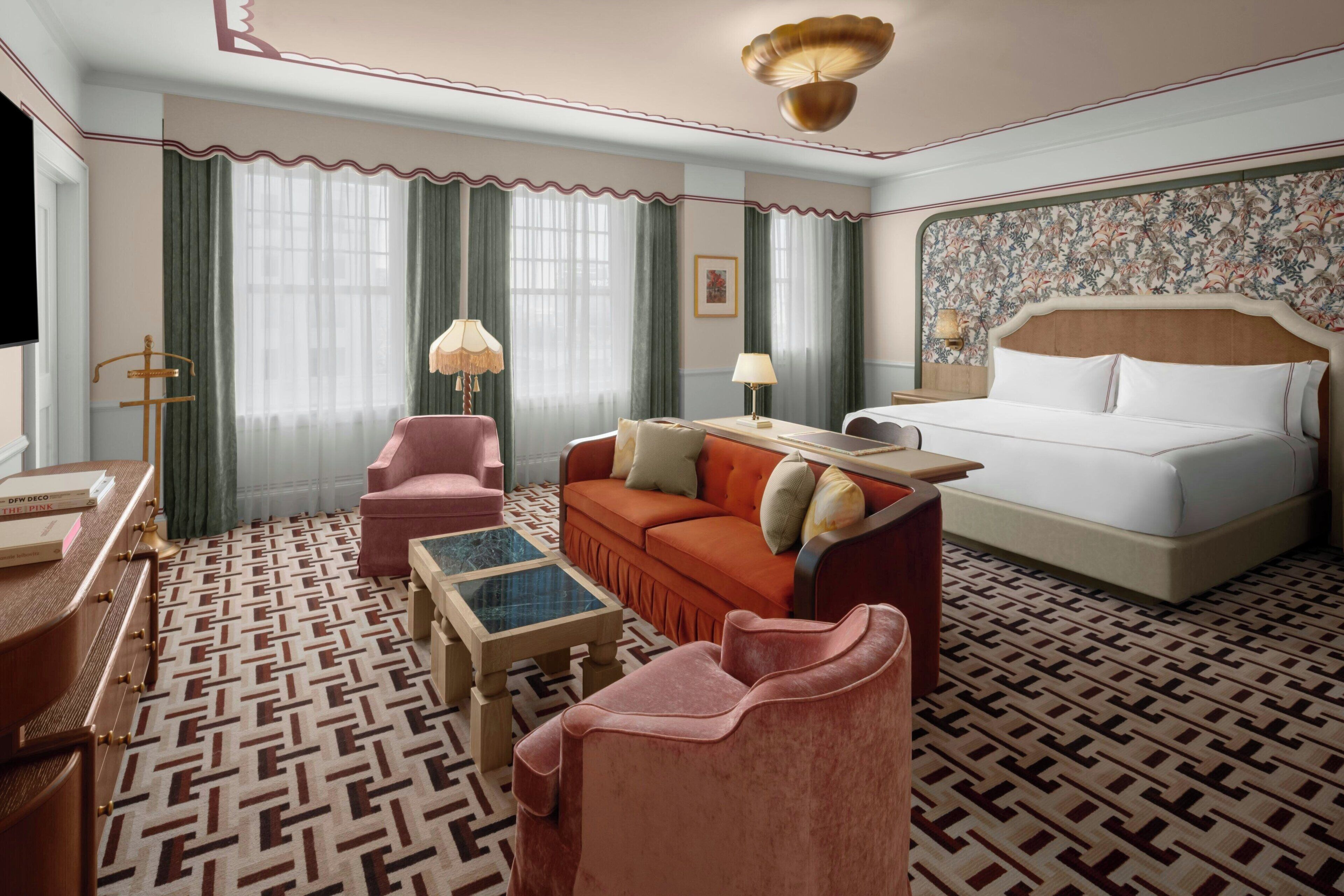 A hotel room with a bed, a sofa, a chair, a coffee table, and a desk with a lamp.