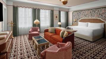 A hotel room with a bed, a sofa, a chair, a coffee table, and a desk with a lamp.