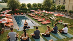 A group of people meditating on yoga mats in a courtyard with a pool, surrounded by lounge chairs and umbrellas. - The Stoneleigh, Autograph Collection (Dallas)