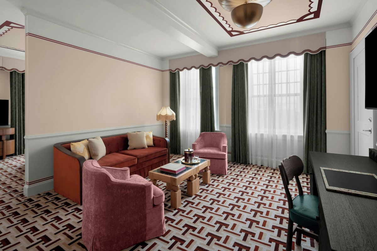 A room with a patterned floor, a sofa, two armchairs, a coffee table, a lamp, and a television.