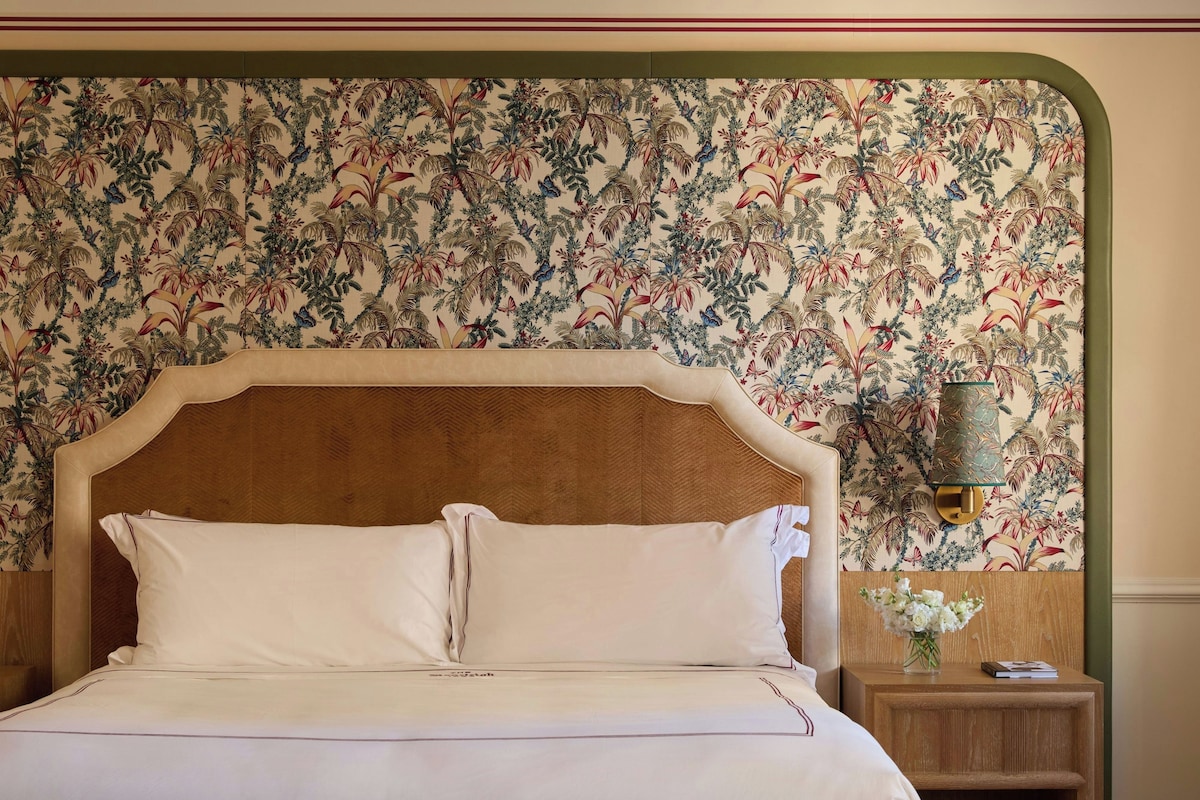 A bed with white linens and a headboard with a floral pattern.