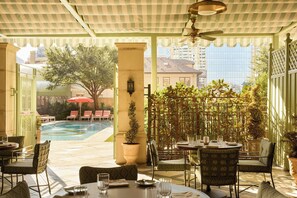 A covered outdoor seating area with tables and chairs, a pool, and a view of the cityscape. - The Stoneleigh, Autograph Collection (Dallas)