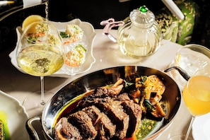 A dining table with a variety of dishes, including a platter of meat and vegetables, and several glasses of wine.