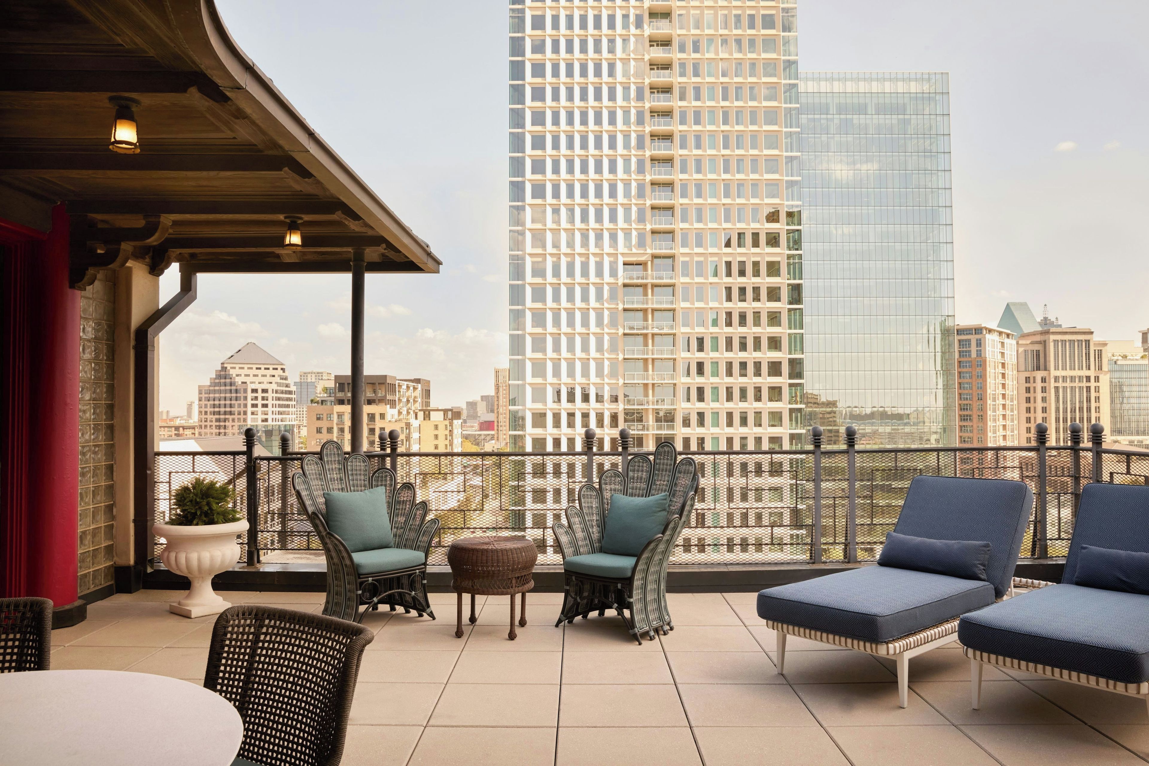 Terraza en la azotea con mobiliario de mimbre, una mesa y vistas a un horizonte urbano.