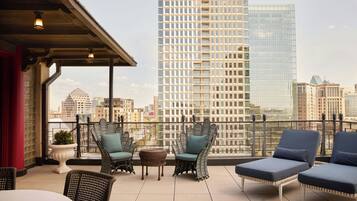 Terraza en la azotea con mobiliario de mimbre, una mesa y vistas a un horizonte urbano.