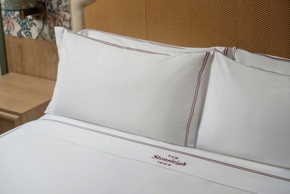 A neatly made bed with white bedding and a pillow with a red stripe.