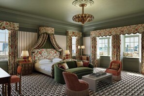 A hotel room with a bed, a green sofa, a red armchair, a patterned floor, and a chandelier.