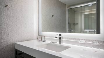 A modern bathroom with a large mirror, two sinks, and a shower visible in the reflection.