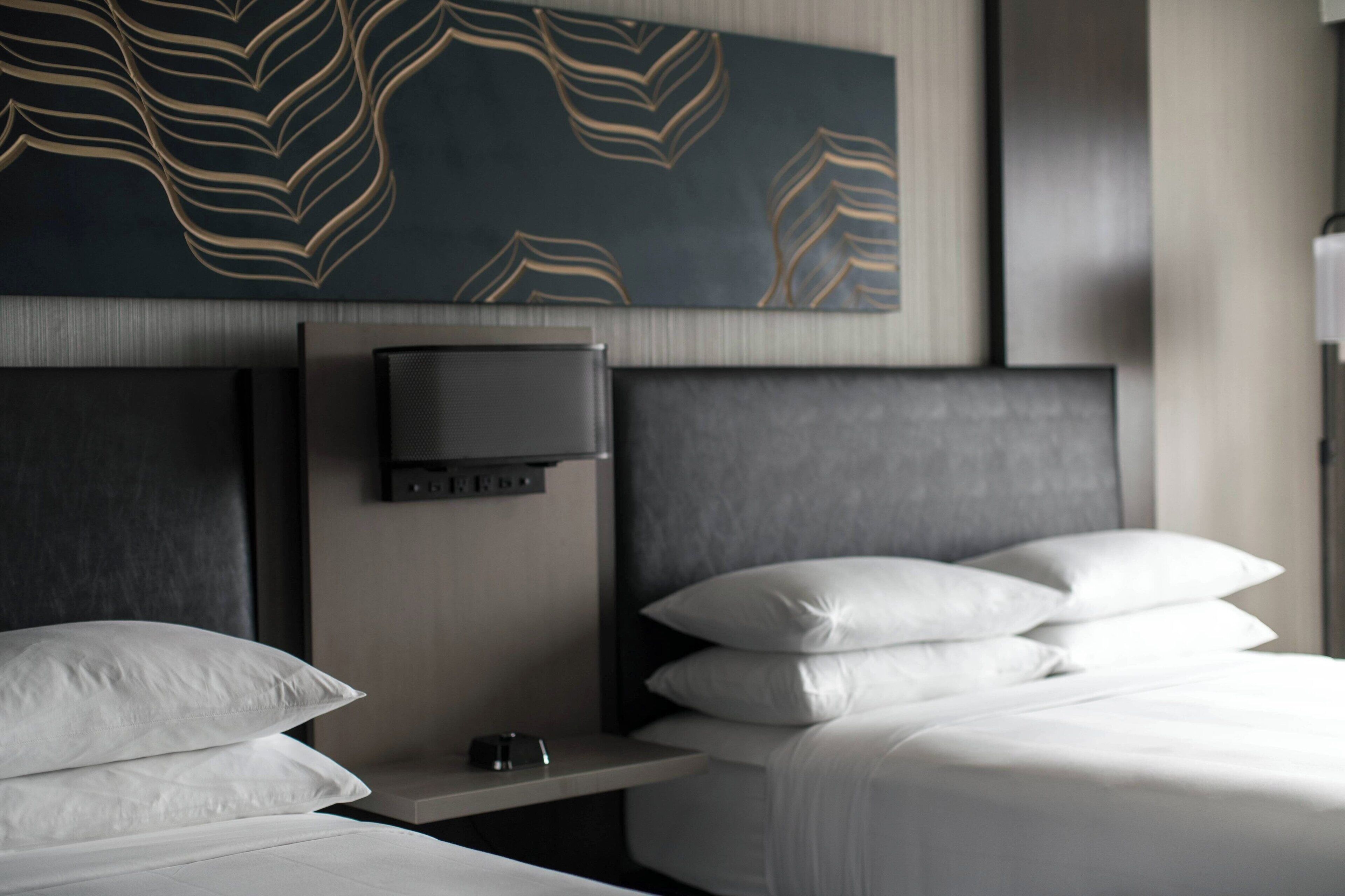 Ein modernes Hotelzimmer mit einem großen Bett, einem Nachttisch mit Flachbildfernseher und einer dekorativen Wandverkleidung.