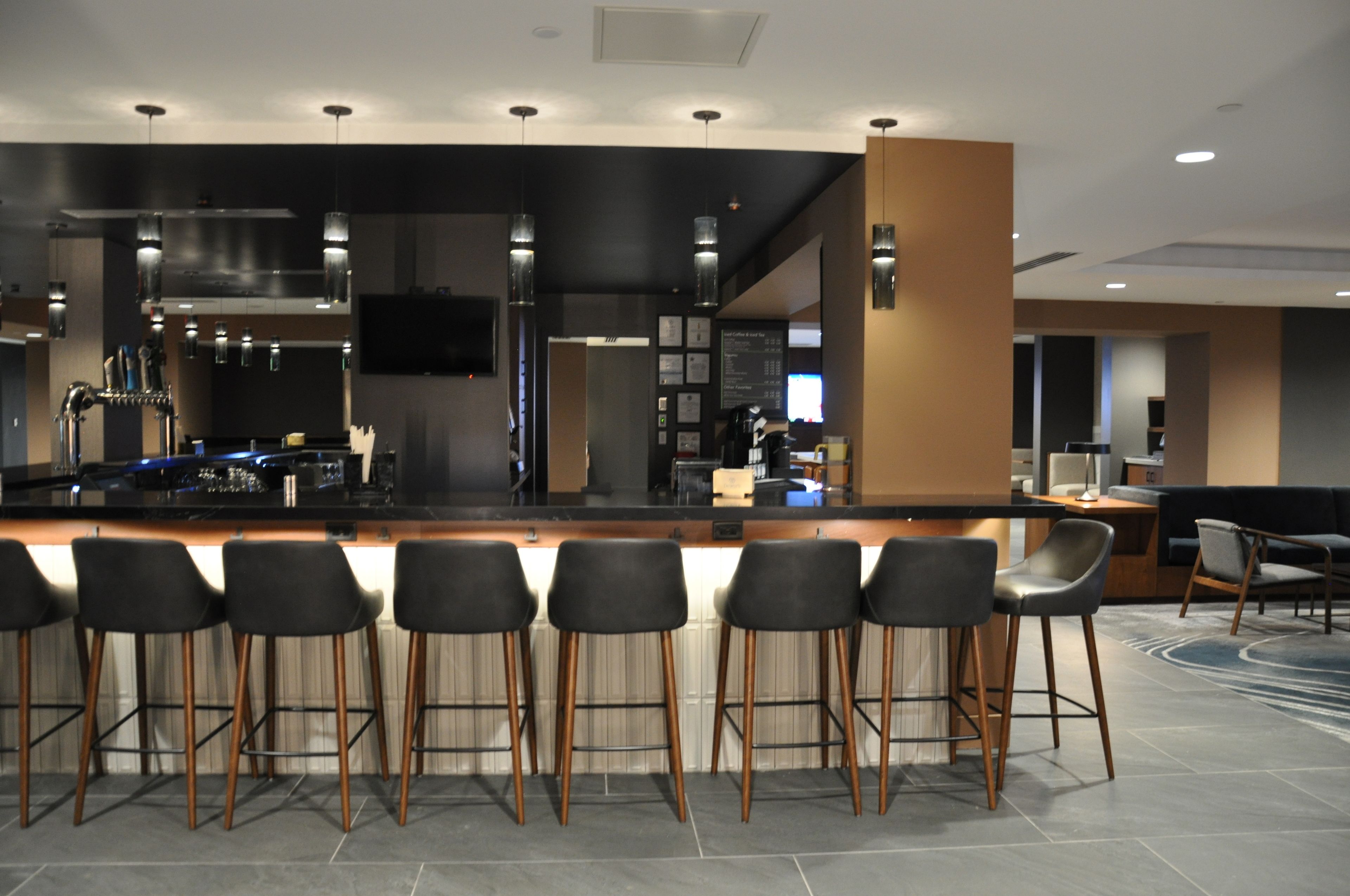 A modern bar area with a long counter, black bar stools, and a television mounted on the wall.