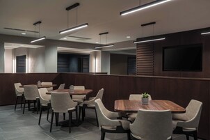 Un comedor moderno con varias mesas y sillas, iluminación empotrada y un televisor de pantalla plana grande montado en la pared.