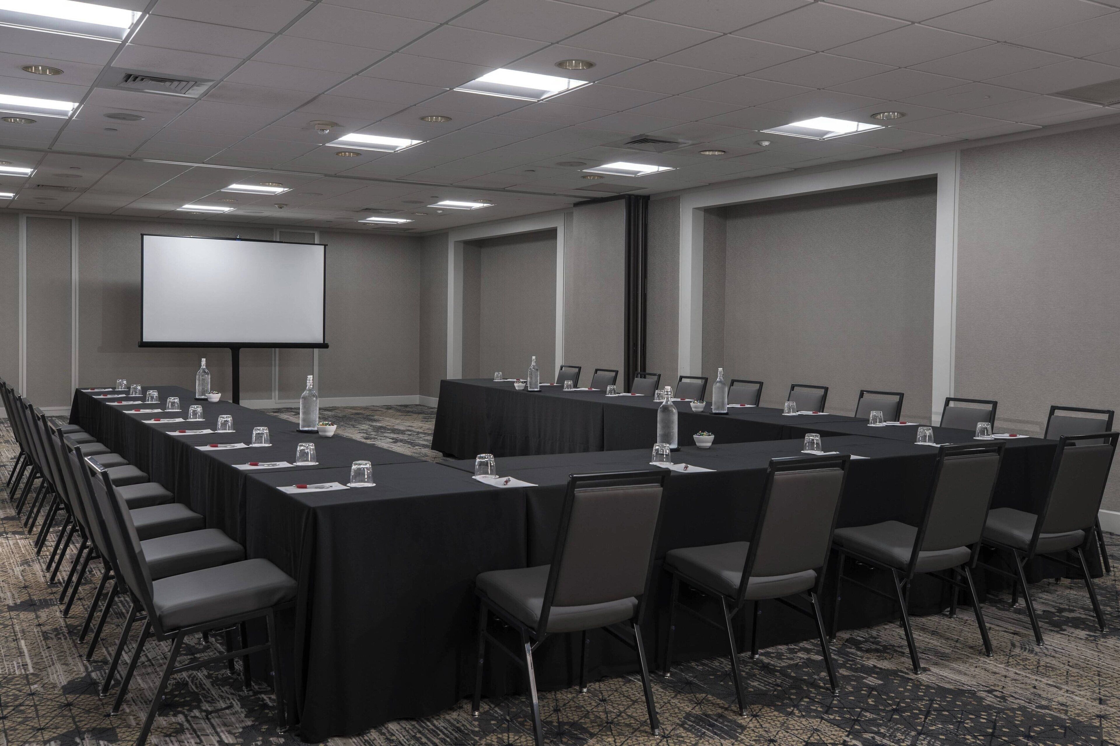 A conference room with a long table, chairs, a projector screen, and a carpeted floor.