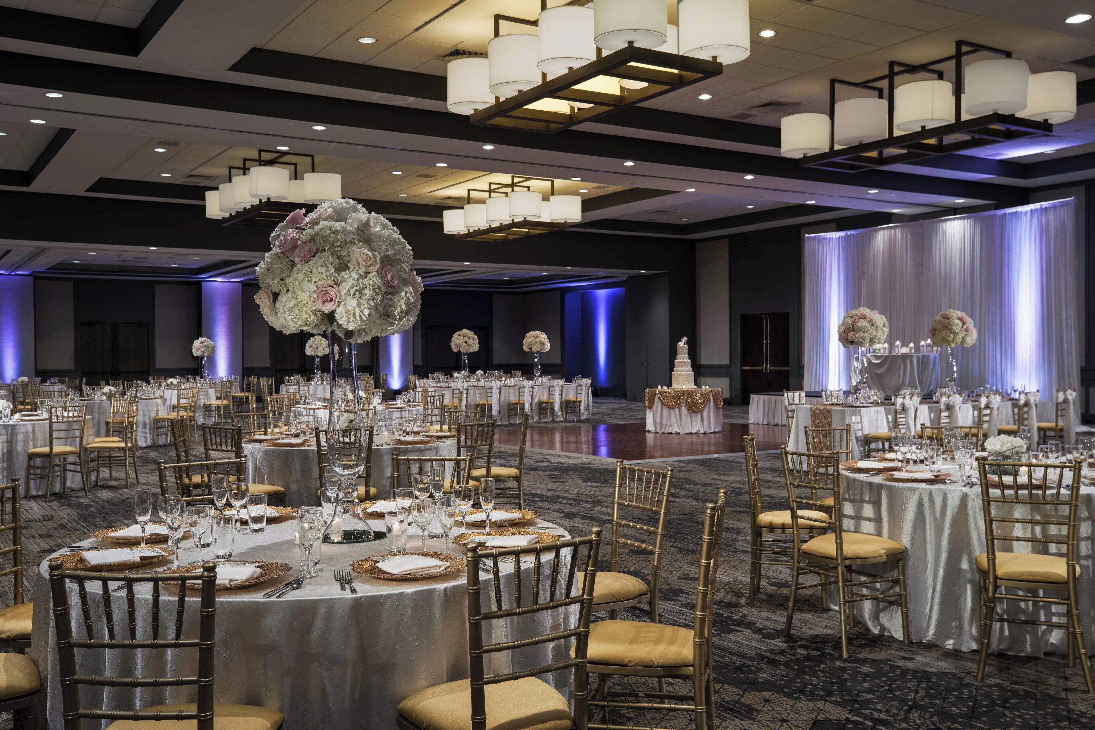 A banquet hall with round tables set for a formal event, featuring gold chairs and white tablecloths.