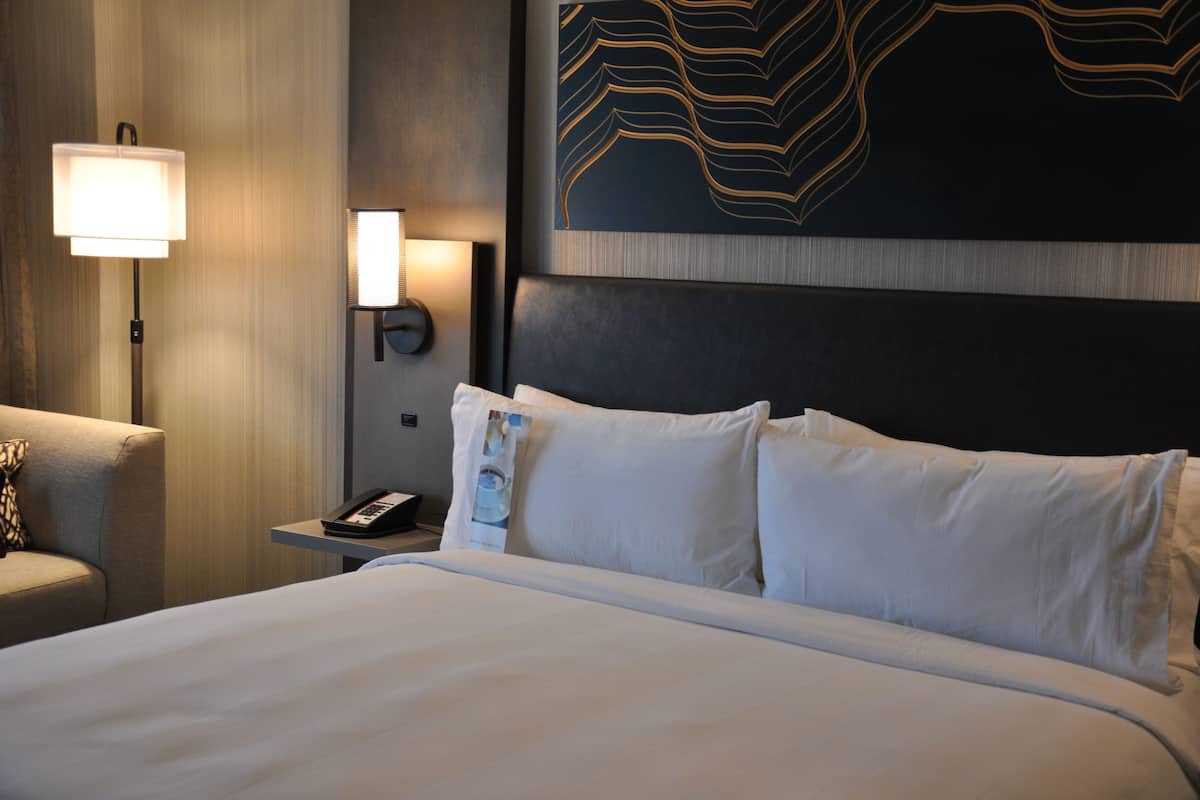Une chambre d’hôtel avec un grand lit, une table de chevet avec une lampe, un téléphone et une œuvre d’art murale.