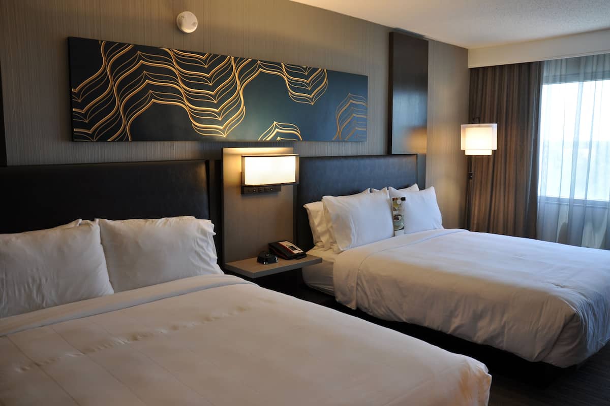 Une chambre d’hôtel avec deux lits, une œuvre d’art accrochée au mur, des lampes de chevet et une fenêtre avec des rideaux.