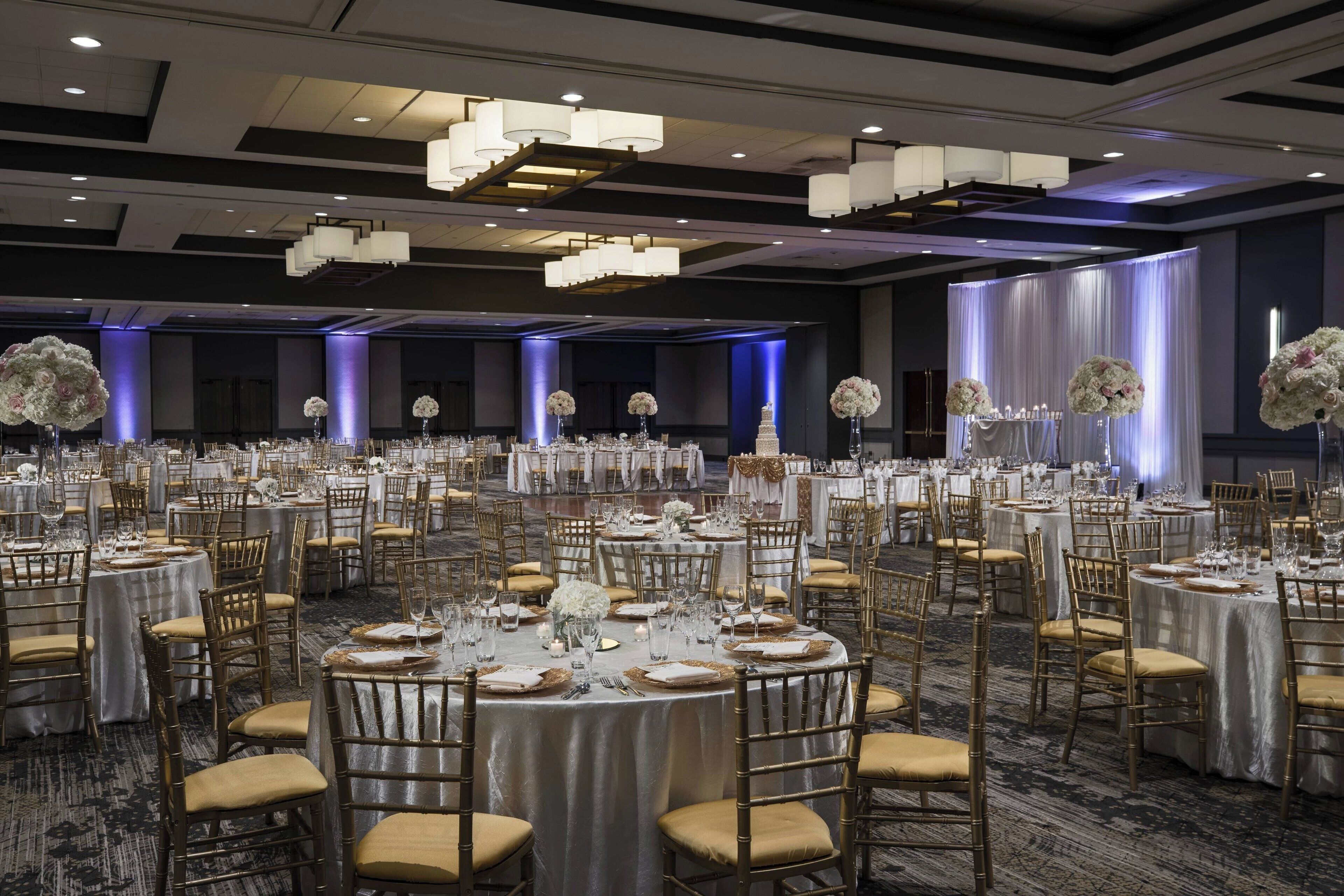 A banquet hall with round tables, gold chairs, and white tablecloths.