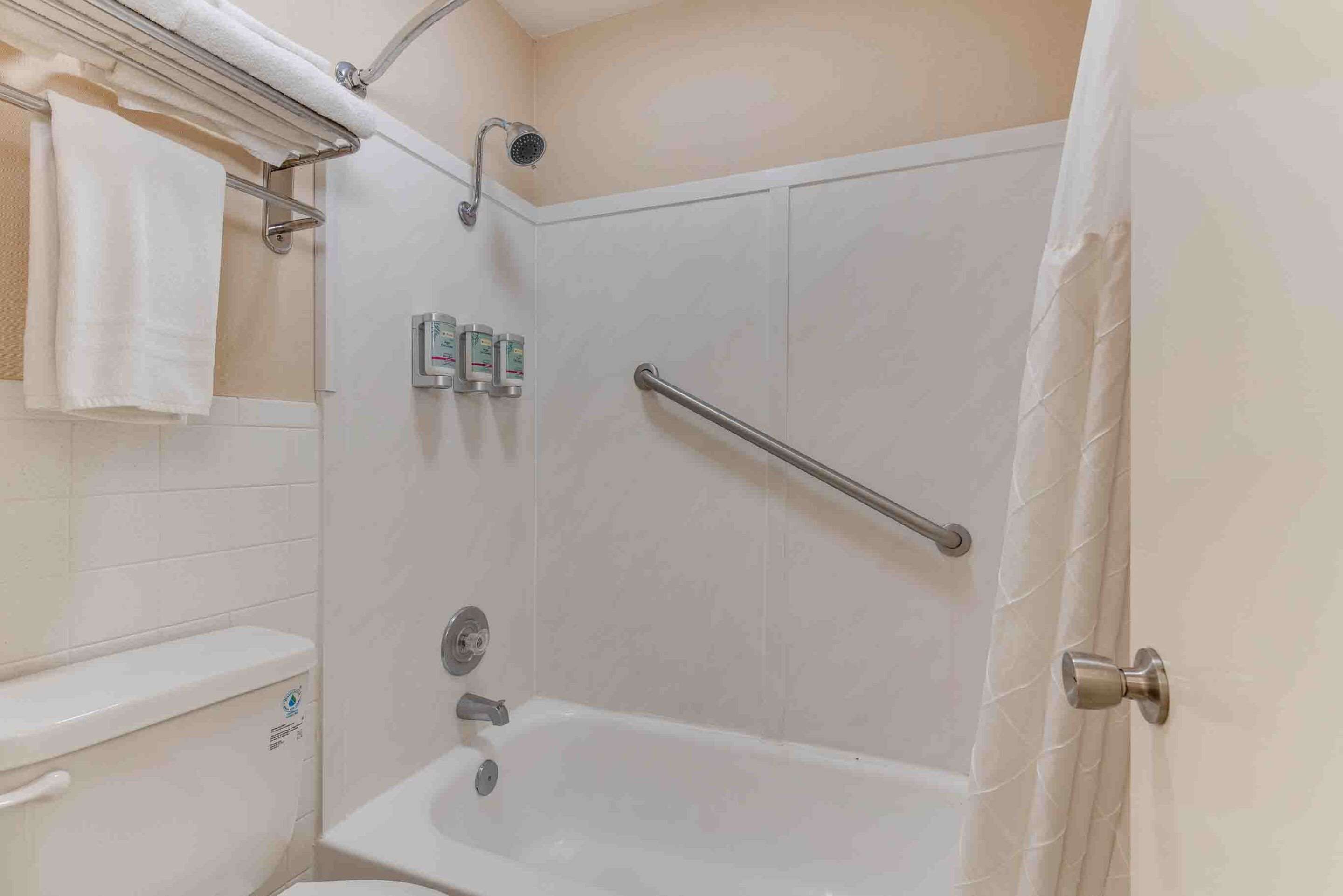 Un baño con ducha, inodoro y barras de apoyo.