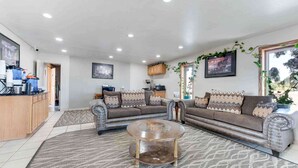 A living room with a sofa set, a coffee table, and a kitchen area with appliances. - Best Western Movie Manor (Monte Vista)