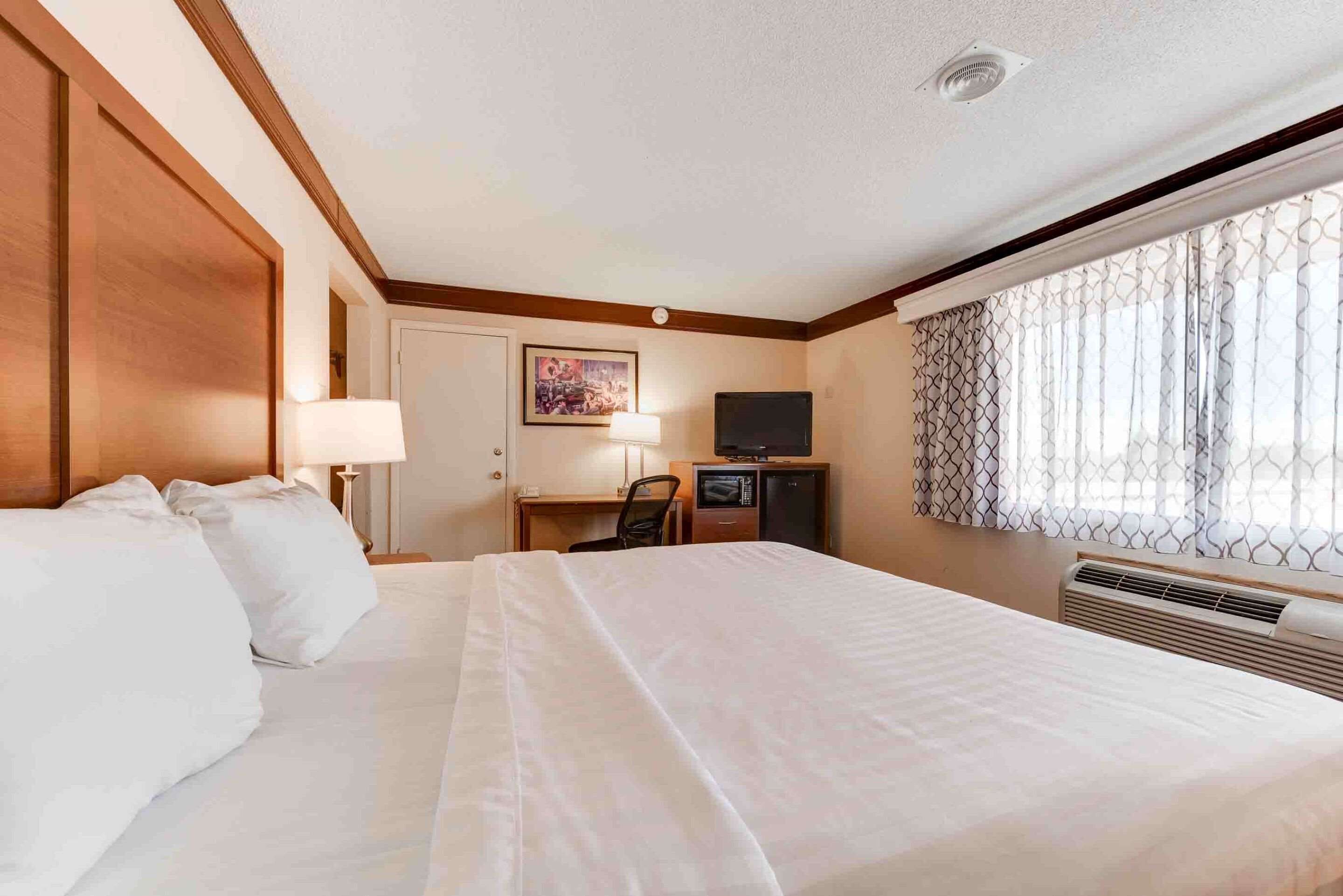 A hotel room with a large bed, a desk with a chair, a television, and a window with a curtain.
