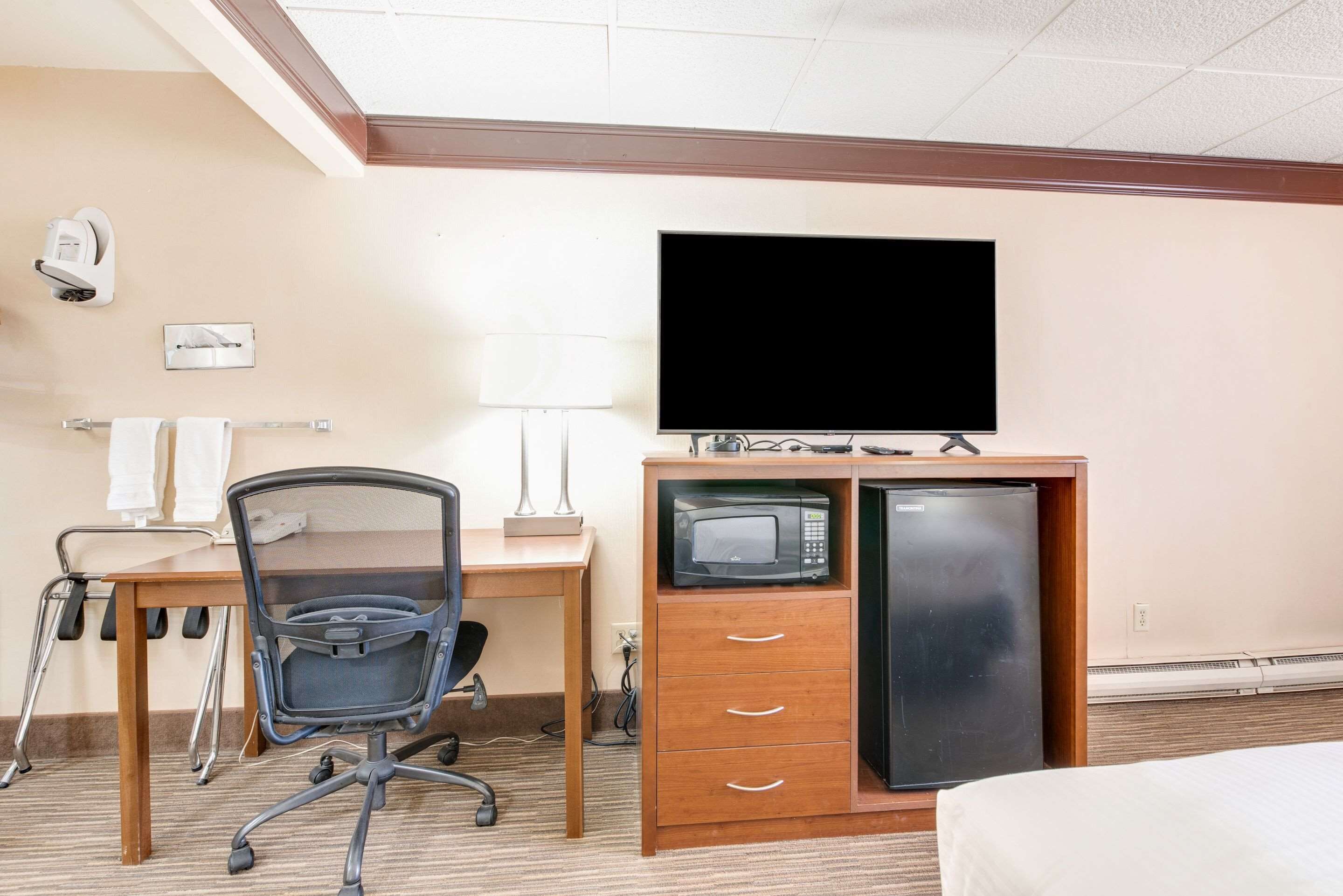 Ein Hotelzimmer mit Schreibtisch, Stuhl, Fernseher, Mikrowelle und Kühlschrank.
