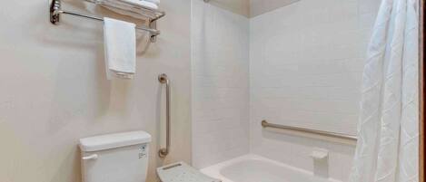 A bathroom with a toilet, a shower with a grab bar, and a small step stool.