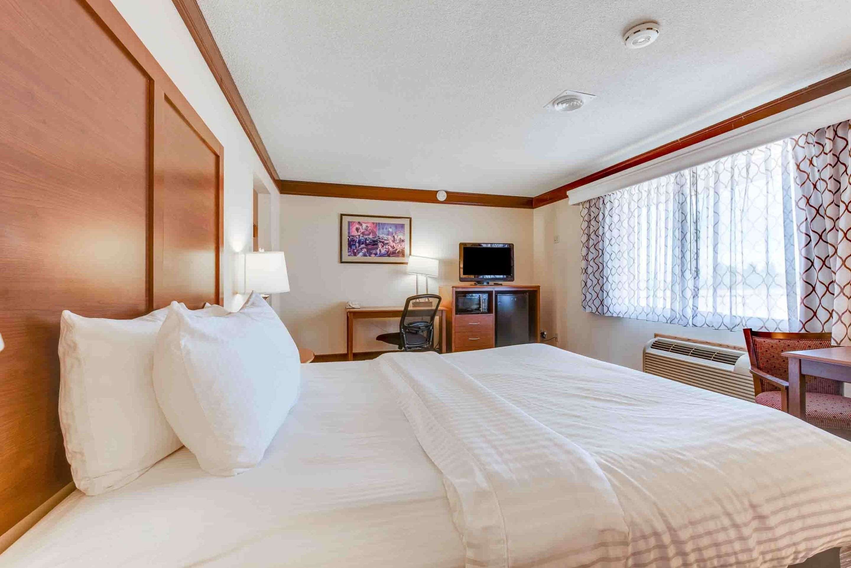 A hotel room with a large bed, a desk with a computer, a TV, and a window with patterned curtains.