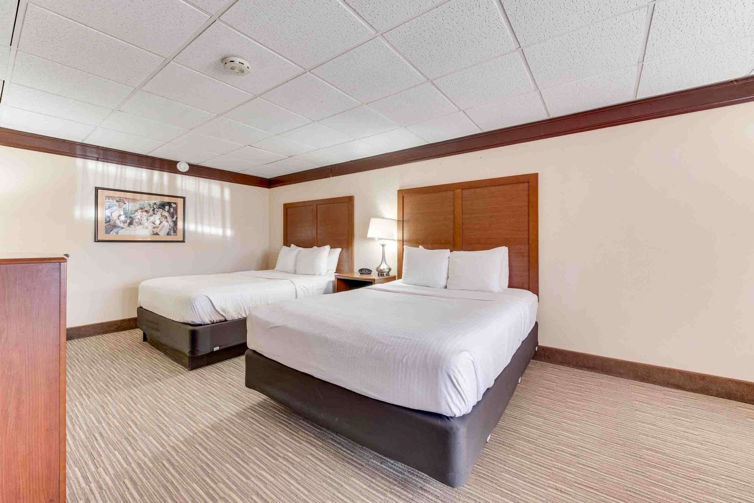 A hotel room with two beds, a desk, a lamp, and a framed picture on the wall.