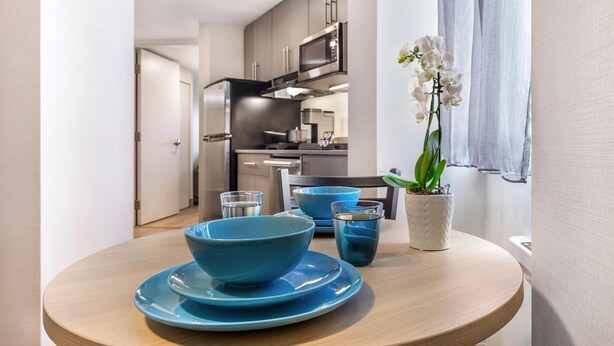 A modern kitchen with grey cabinets, a stainless steel refrigerator, and a microwave. There is a dining table with blue plates and a potted orchid. - Best Western Plus Ottawa City Centre (Ottawa)