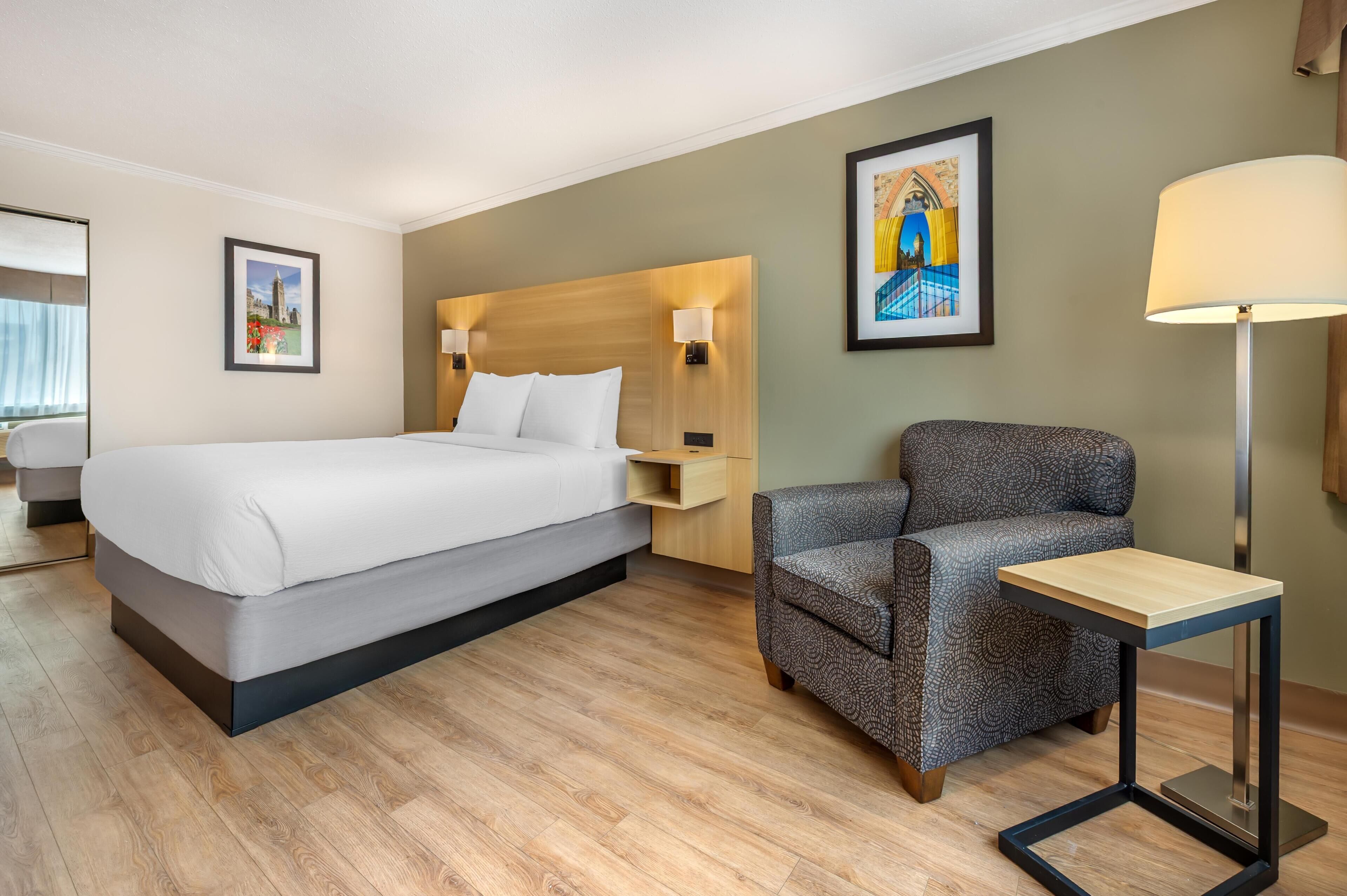 A modern hotel room with a large bed, a patterned armchair, a small table, and two wall-mounted lamps.