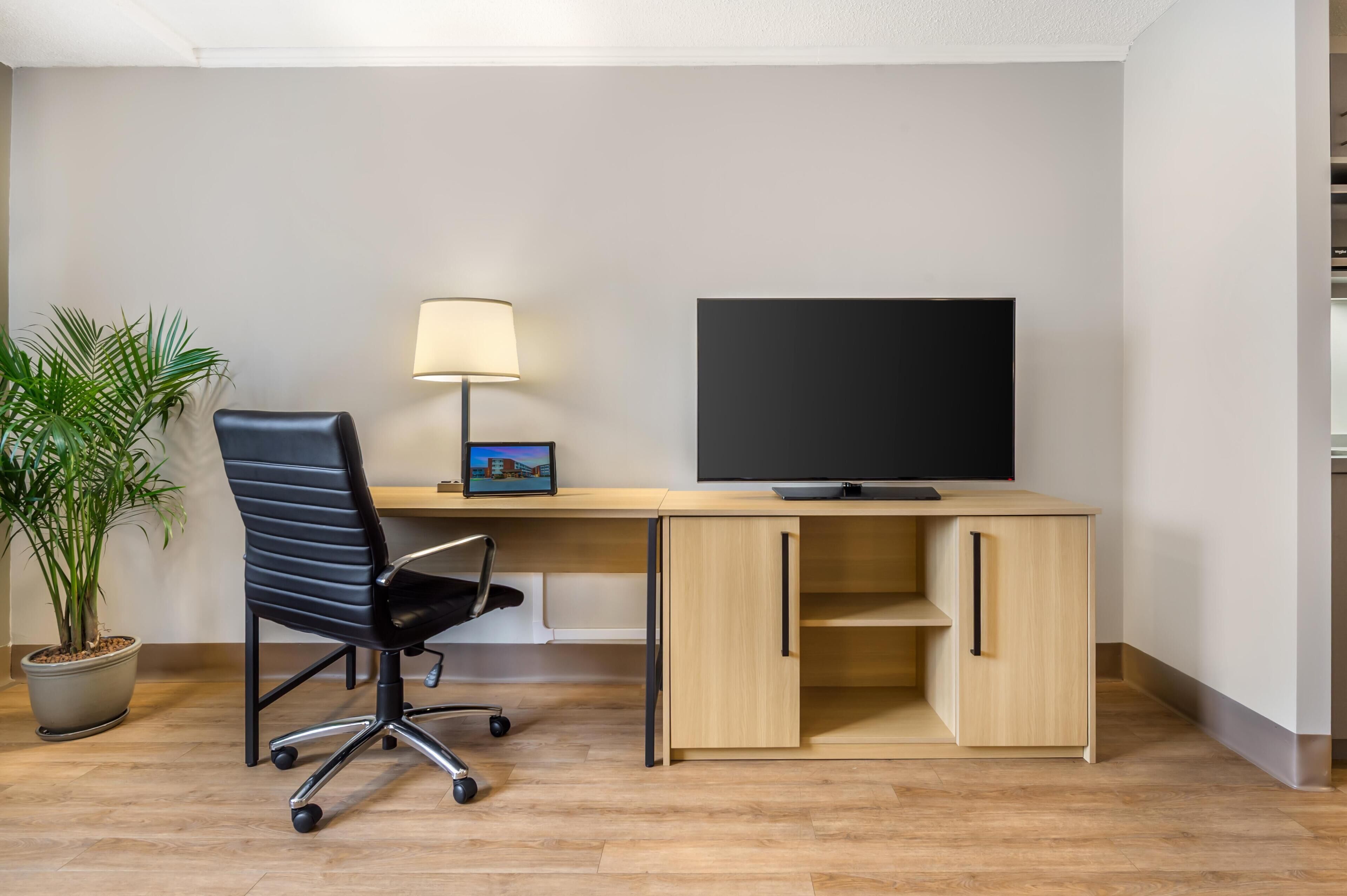 A modern office space with a desk, chair, lamp, and a large flat-screen TV.