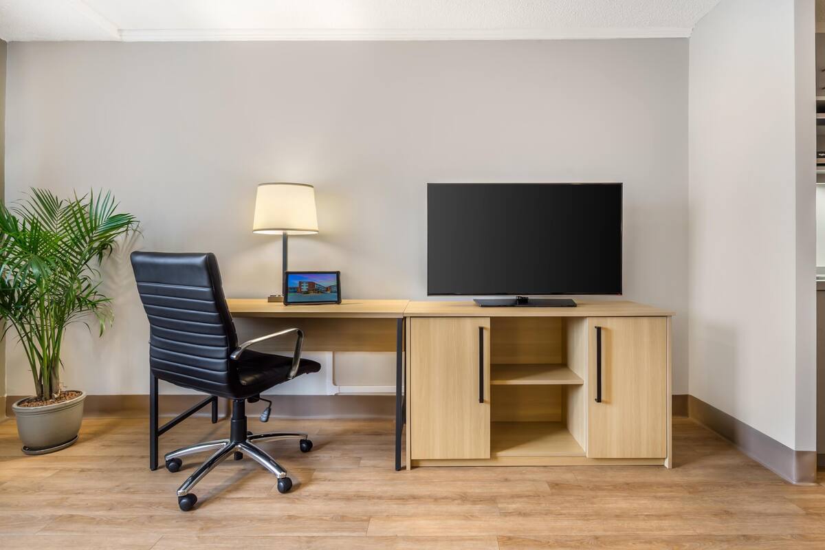 A modern office space with a desk, chair, lamp, and a large flat-screen TV.