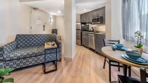 A compact living space with a sofa, a dining table with blue plates, a kitchen area with modern appliances, and a potted plant. - Best Western Plus Ottawa City Centre (Ottawa)