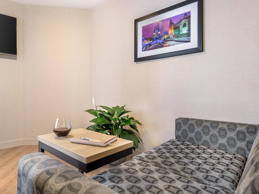 Una sala de estar moderna con un sofá, una mesita con una copa de vino, una planta y un cuadro en la pared.
