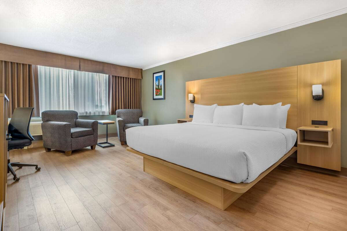 A hotel room with a large bed, two armchairs, a desk, and a window with curtains.