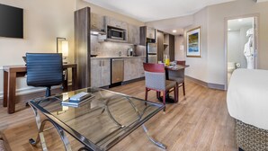 A modern hotel room with a glass dining table, a blue office chair, a red patterned chair, a bed, and a kitchenette. - Best Western Plus Ottawa City Centre (Ottawa)