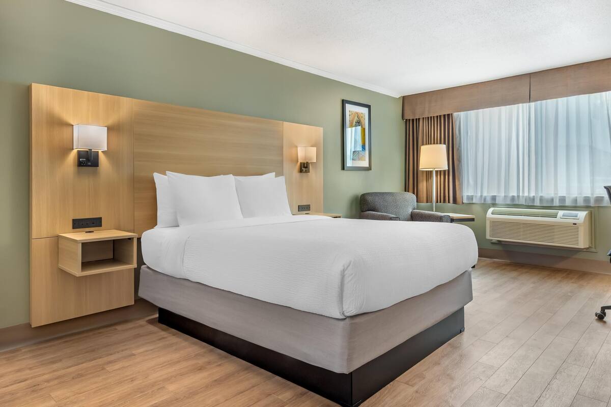 A modern hotel room with a large bed, bedside lamps, a chair, and a window with curtains.