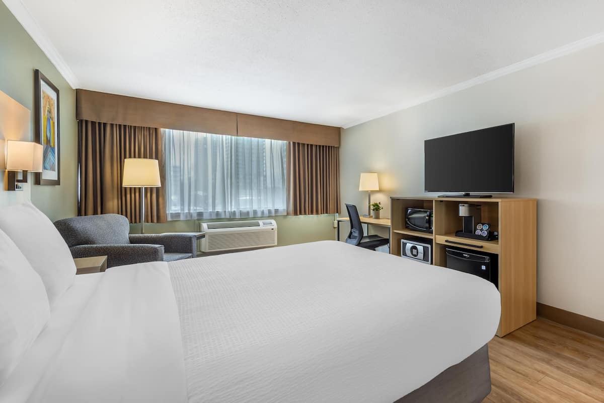 Une chambre d’hôtel dotée d’un grand lit, d’un bureau avec un ordinateur, d’une télévision à écran plat, d’un four à micro-ondes et d’un mini-réfrigérateur.