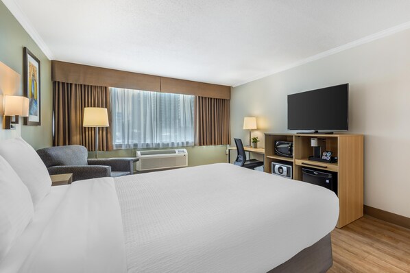 Habitación de hotel con una cama grande, un escritorio con computadora, un televisor de pantalla plana, un microondas y un refrigerador pequeño.