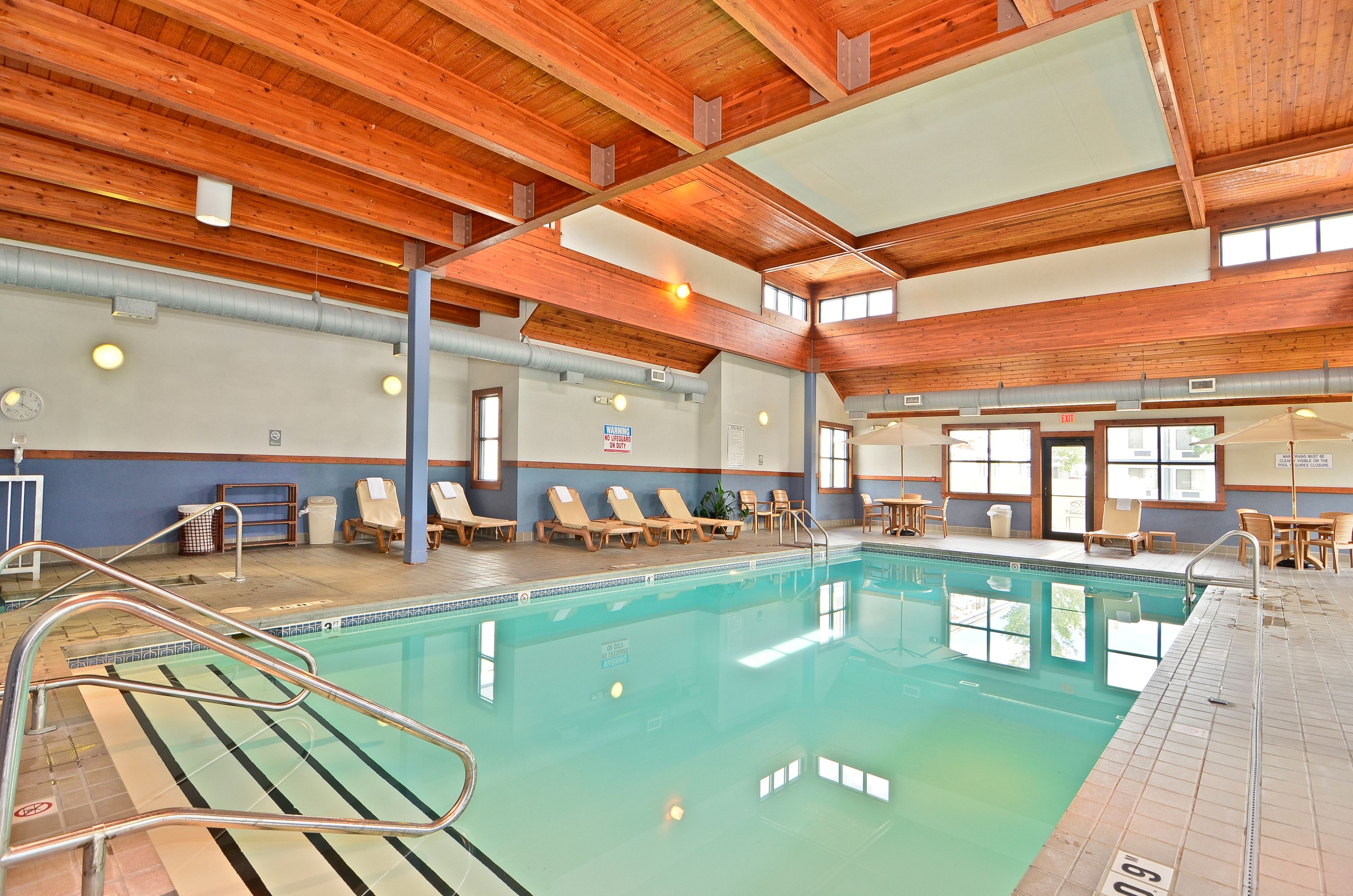 An indoor swimming pool with wooden beams, lounge chairs, and a tiled floor.