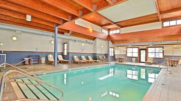An indoor swimming pool with wooden beams, lounge chairs, and a tiled floor.