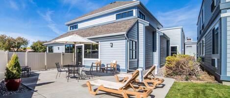 A two-story house with a patio area featuring outdoor furniture and a small garden.